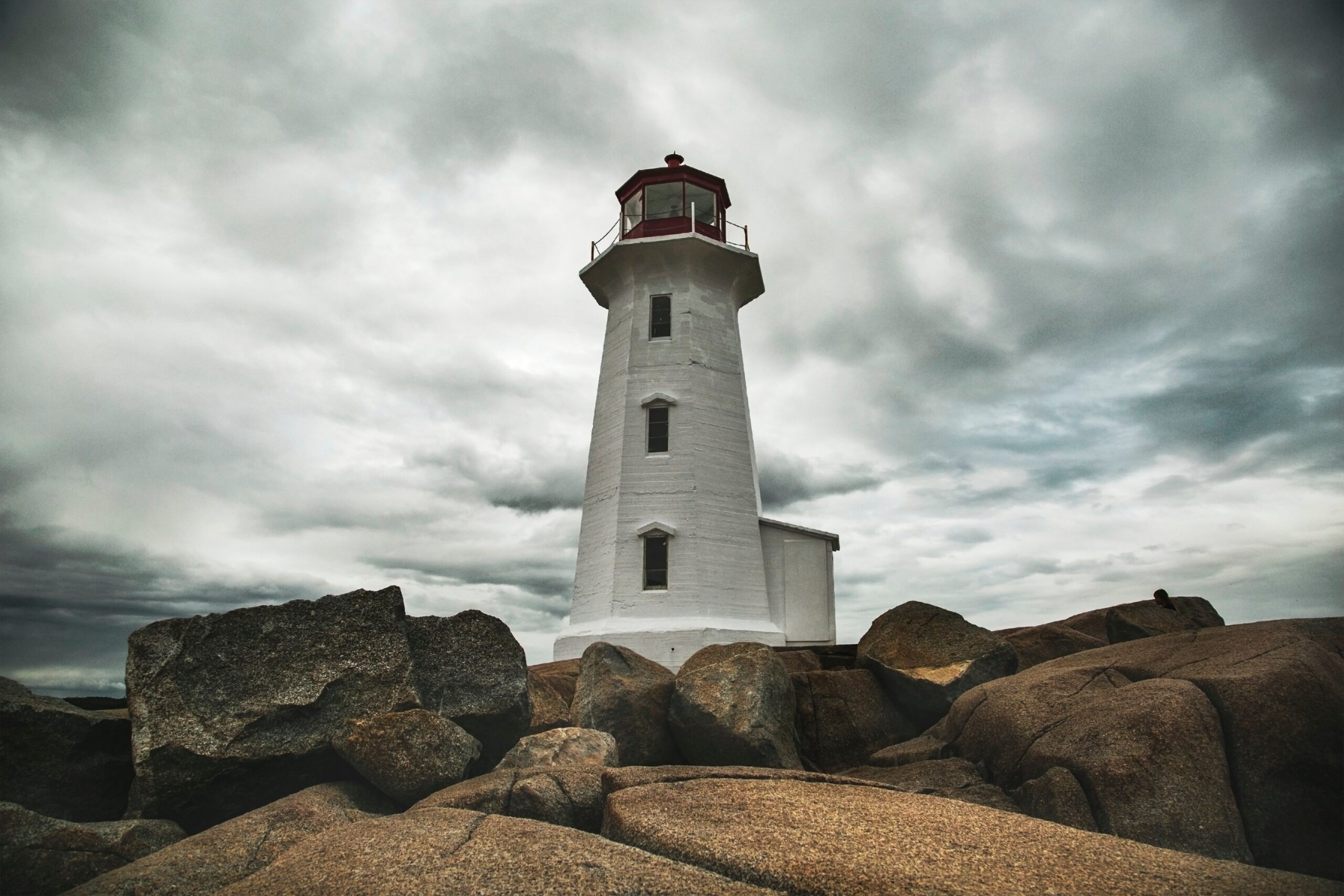 Lighthouse on a rocky shoreline in Nova Scotia under cloudy skies.