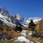 Snow-covered mountain peaks rising above a forested valley with autumn trees and a natural walking path