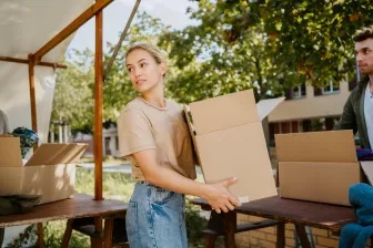 Single mother in a tan shirt and blue jeans carrying a moving box into a new apartment