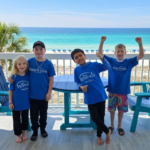 Children wearing Make-A-Wish Canada shirts smiling on a beach balcony during a wish trip supported by Blue Cross