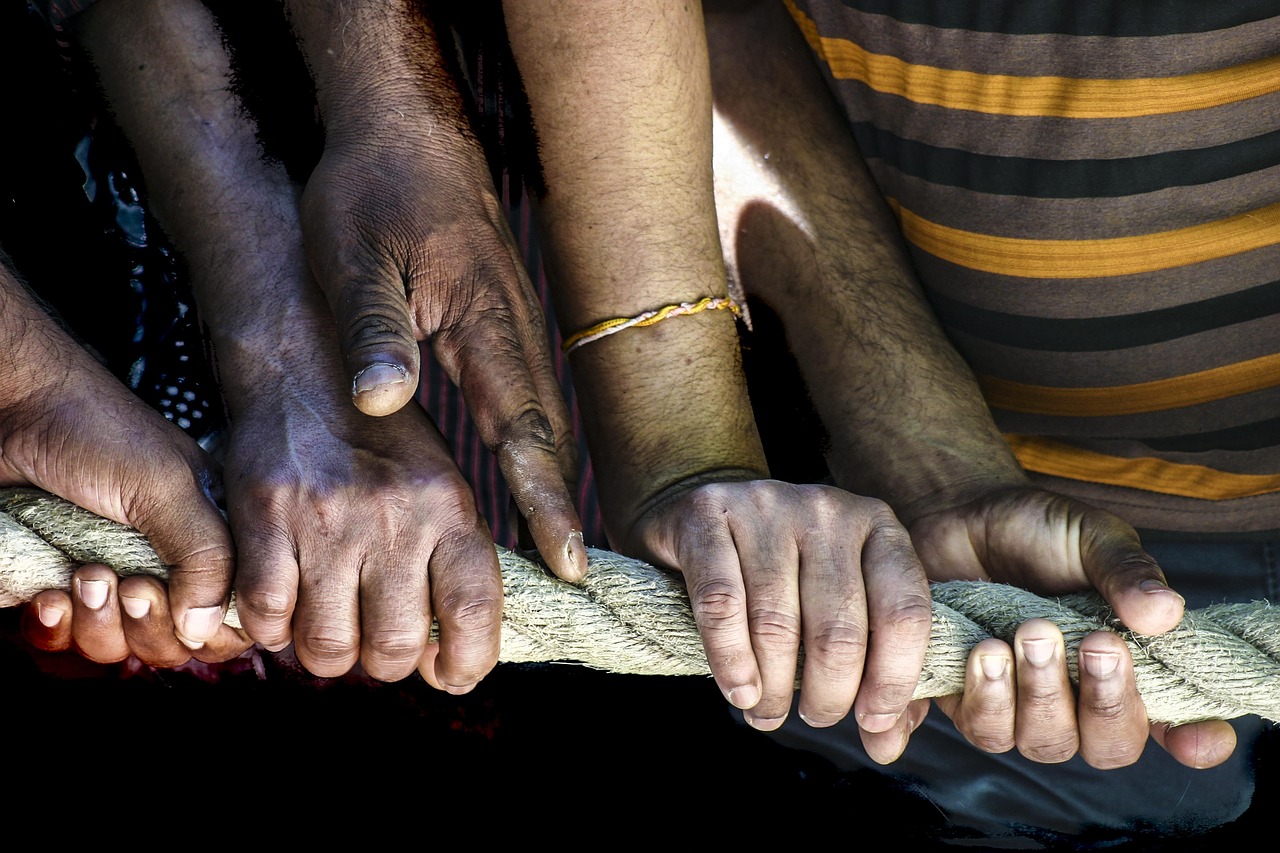 Diverse hands gripping a rope together, symbolizing teamwork and community support within an Alberta addiction recovery charity program.