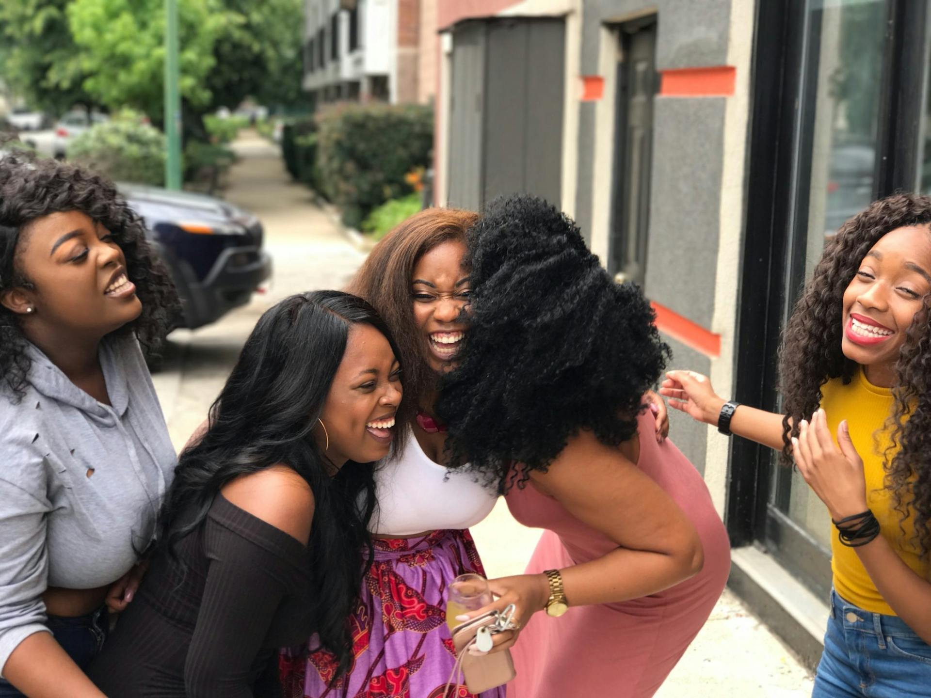 Five Black women smiling and spending time together outdoors in a bright natural setting.