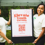 Two volunteers display an Elevate Youth Toronto sign promoting mentorship, career readiness, and youth development programs.