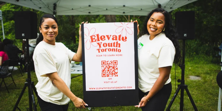Two volunteers display an Elevate Youth Toronto sign promoting mentorship, career readiness, and youth development programs.